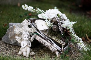 Engel neben Trauergebinde aus Birkenrinde weißen Rosen und Tannenzapfen